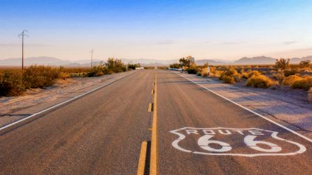 A wide desert road at sunset with utility poles and the painted words &ldquo;SPEED LIMIT 65&rdquo; on the asphalt.