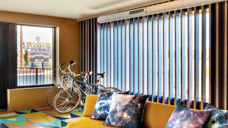 Bright modern living room with galaxy pillows, a bicycle by the window, colorful rug, and vertical blinds.