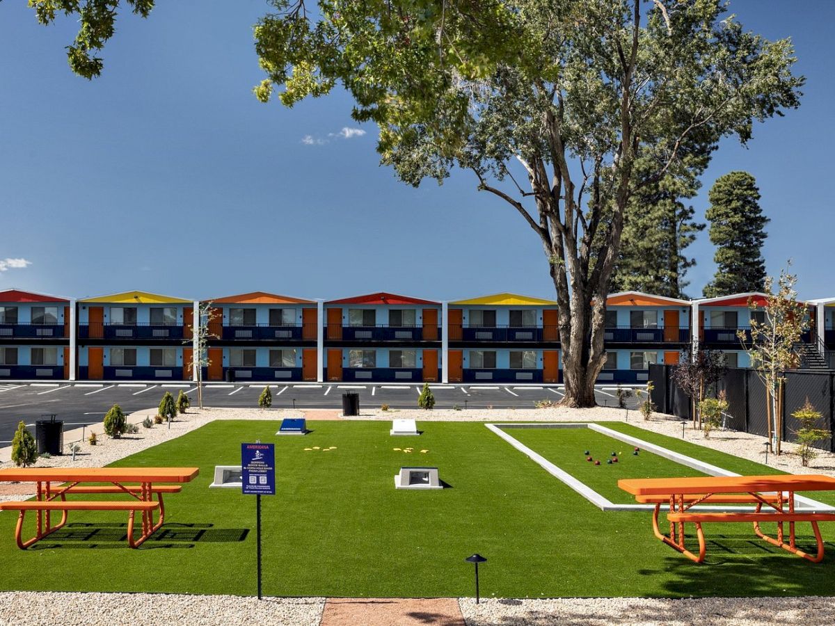 Courtyard with a green lawn, orange benches, a lawn-game area, and colorful two-story rooms under a blue sky.