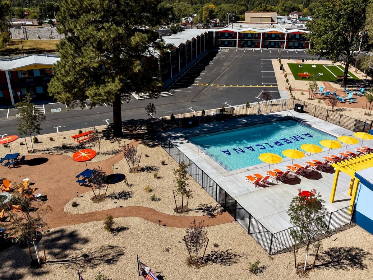 Aerial view of a school campus with a large outdoor swimming pool, lounge chairs, parking lot, and classroom buildings.