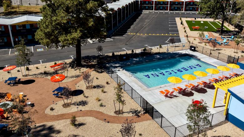 Aerial view of a school campus with a large outdoor swimming pool, lounge chairs, parking lot, and classroom buildings.