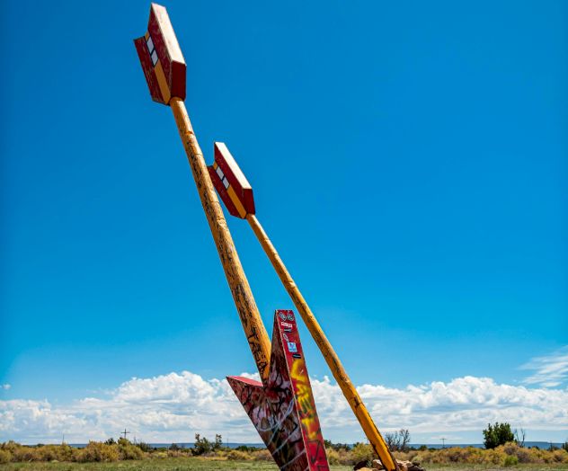 Graffiti-covered wooden signposts leaning in a field beneath a bright blue sky.