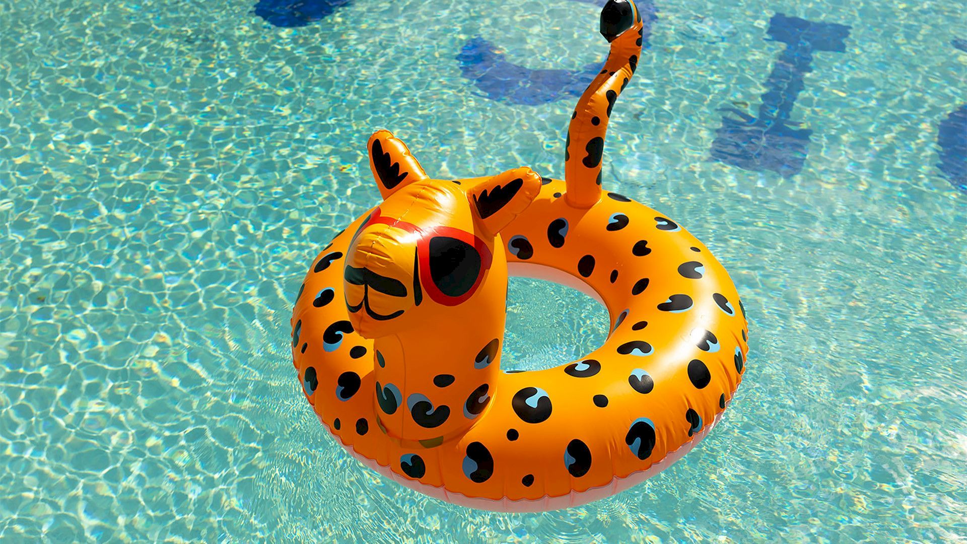 An orange inflatable swim float shaped like a giraffe/life preserver floats in a clear blue pool.